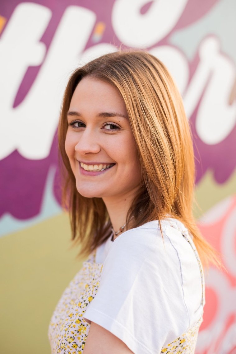 head and shoulders portrait of a high school senior girl standing in front of a colorful mural on the outside wall of the classen inn in midtown Oklahoma City smiling over her shoulder