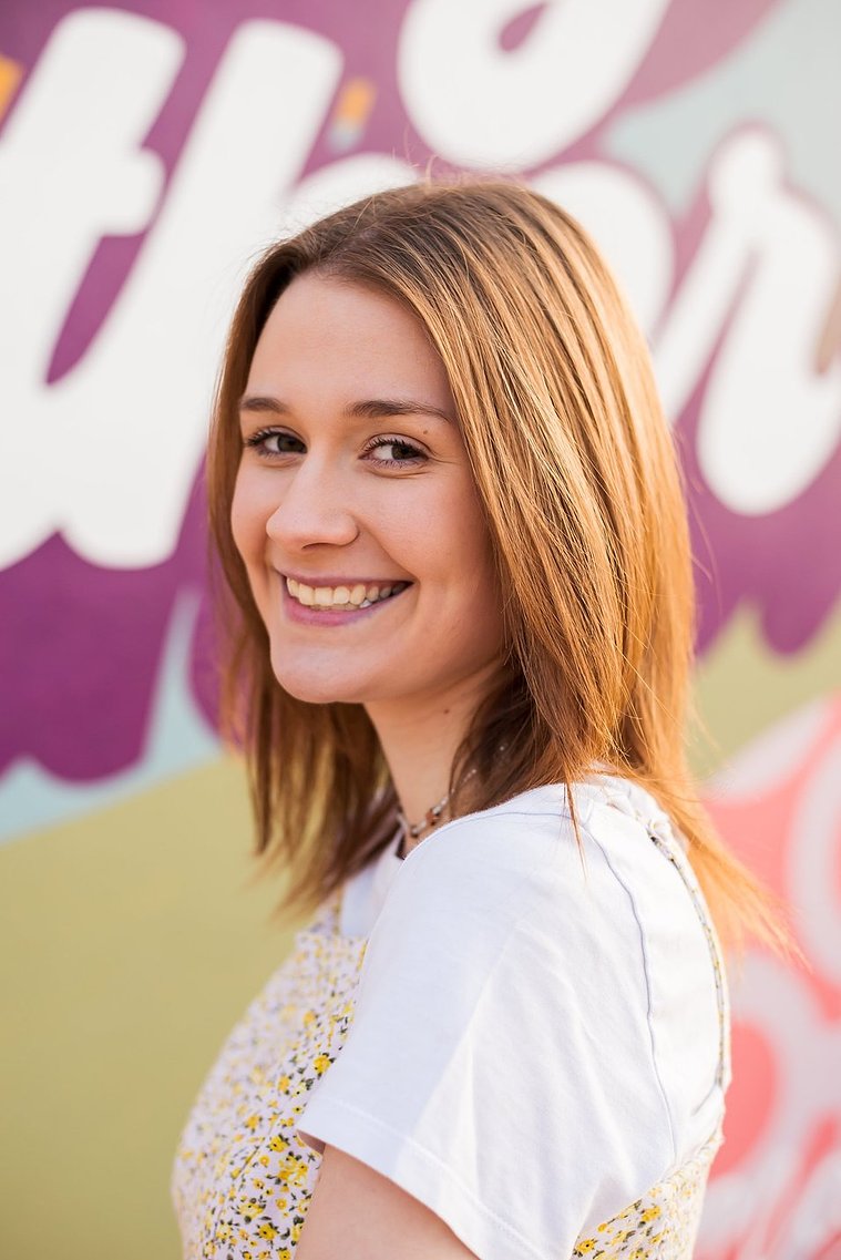 head and shoulders portrait of a high school senior girl standing in front of a colorful mural on the outside wall of the classen inn in midtown Oklahoma City smiling over her shoulder