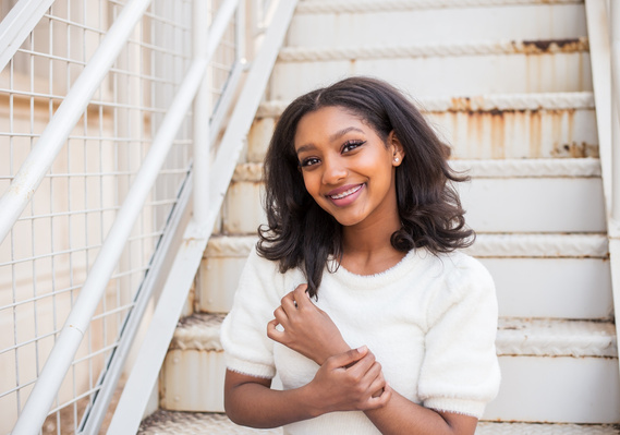 Senior girl sits on steps and smiles at her senior portrait session in Norman, Oklahoma