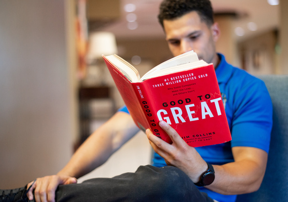 A young male entrepreneur is sitting in a chair in a lobby reading a book called 