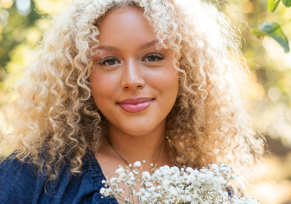 close up portrait of a high school senior girl with blonde curly hair and blue eyes holding a bouquet of baby's breath and smiling softly at Martin Nature Park in Oklahoma City