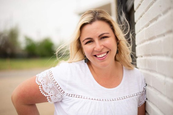 Lifestyle headshot of Cheryl Jackson, a senior portraits and personal branding photographer based in Oklahoma City, Oklahoma. She is wearing a white top and leaning against a white brick wall.