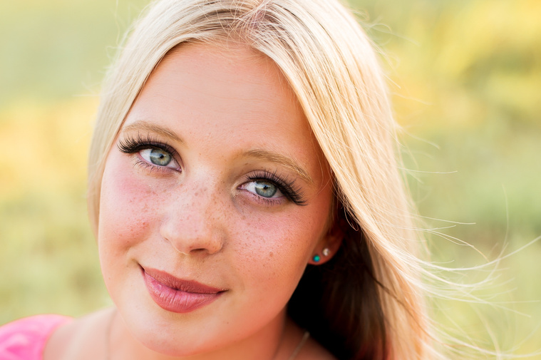 Close up image of a High school senior girl with blond hair and blue eyes smiling softly while she sits in a field in central Oklahoma for her senior photos