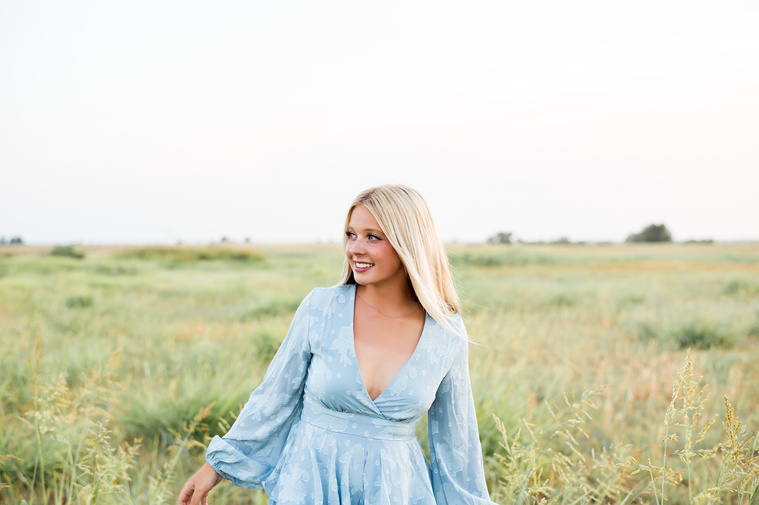 High school senior girl looks off camera while she walks through a field in central Oklahoma for her senior photos