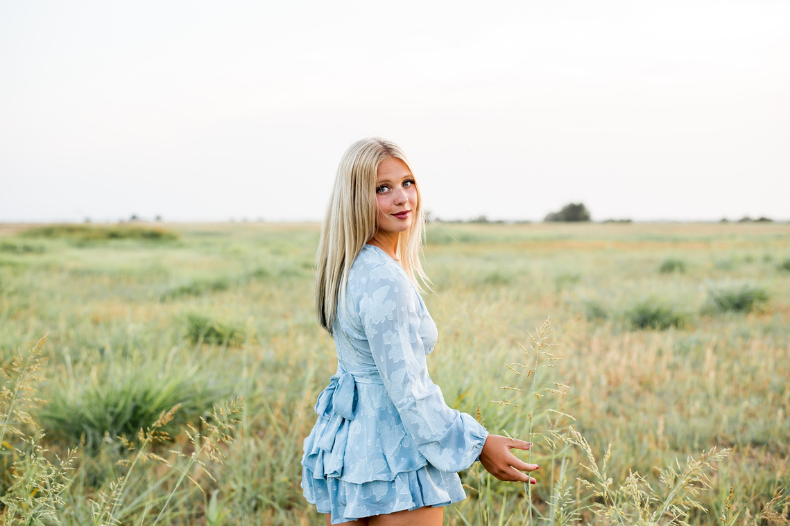 High school senior girl looks over her shoulder while she walks through a field in central Oklahoma for her senior photos