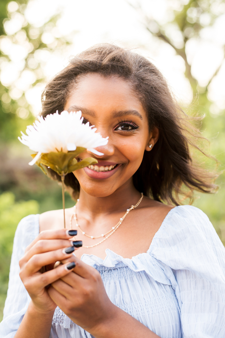 Senior girl poses holding a flower in a grassy field in Oklahoma for a country photo session