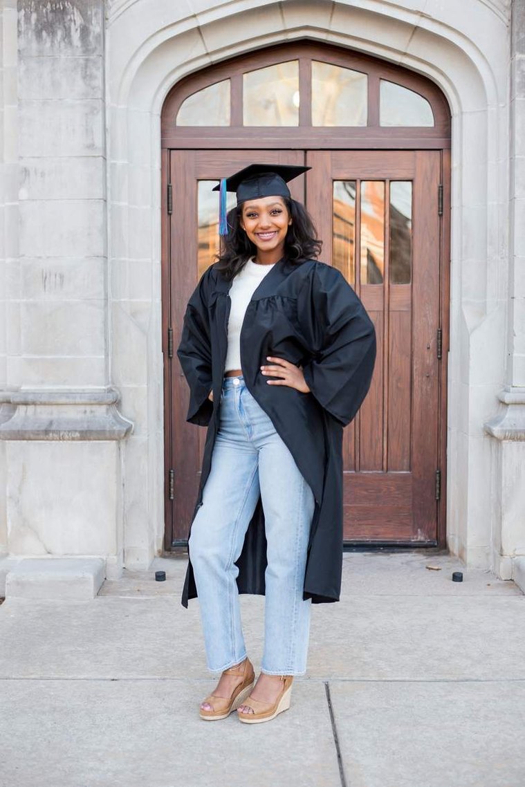 African-American teenage girl stands on the OU campus and smiles in her cap and gown at her senior photo shoot in Norman Oklahoma