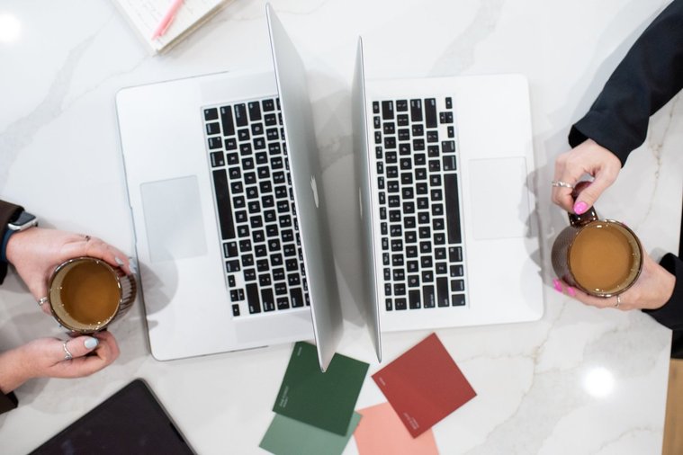 shot from above flat lay branding image of two laptops back to back with color swatches around and two girls on each side of frame holding coffee cups. 