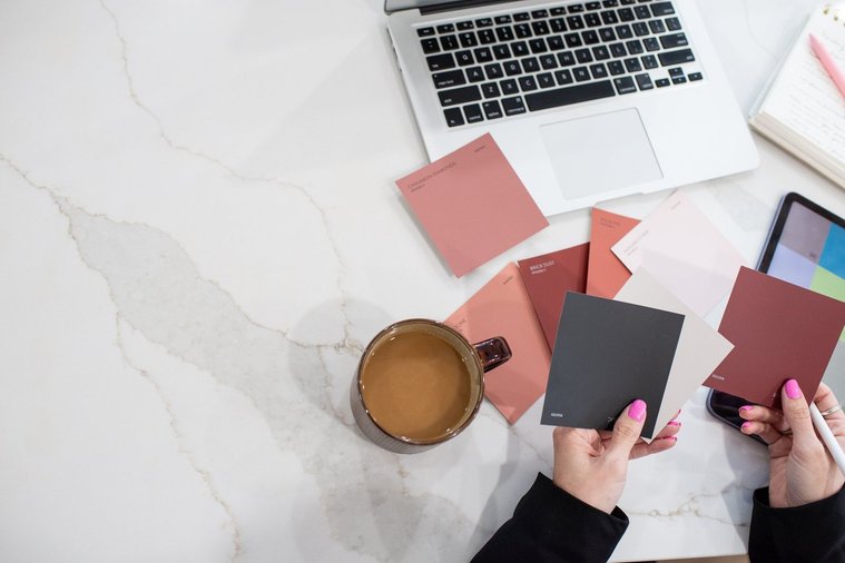 close up image of a designer comparing color swatch options with her laptop, notebook and cup of coffee around at a graphic design team branding session in OKC
