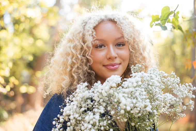close up portrait of a high school senior girl with blonde curly hair and blue eyes holding a bouquet of baby's breath and smiling softly at Martin Nature Park in Oklahoma City