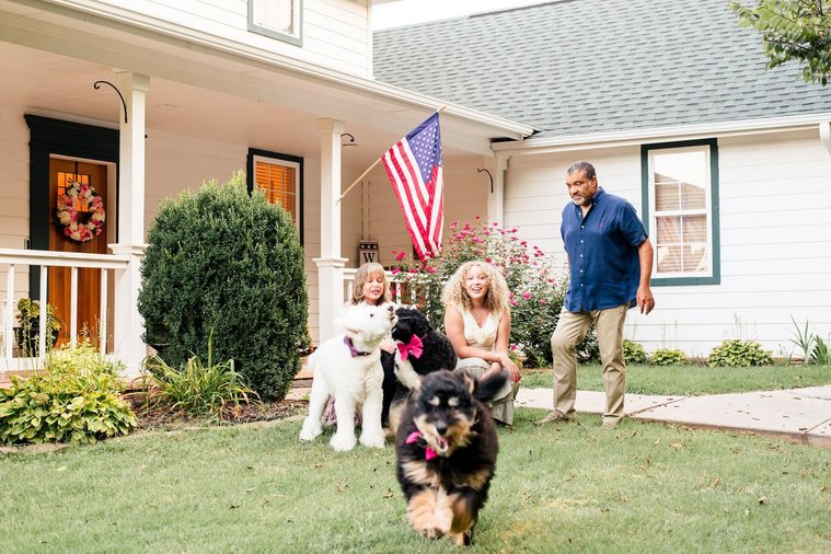 a mom, dad, and teen daughter attempt to sit together with their dogs and pose but one dog is loose and running towards the camera in their yard at their house in Norman, Oklahoma