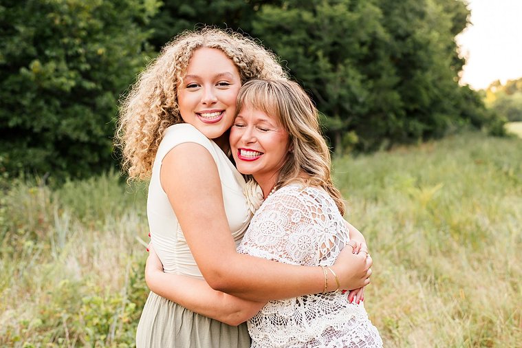 a mom and teen daughter stand together hugging each other and smiling in a field with trees behind them in Norman, Oklahoma