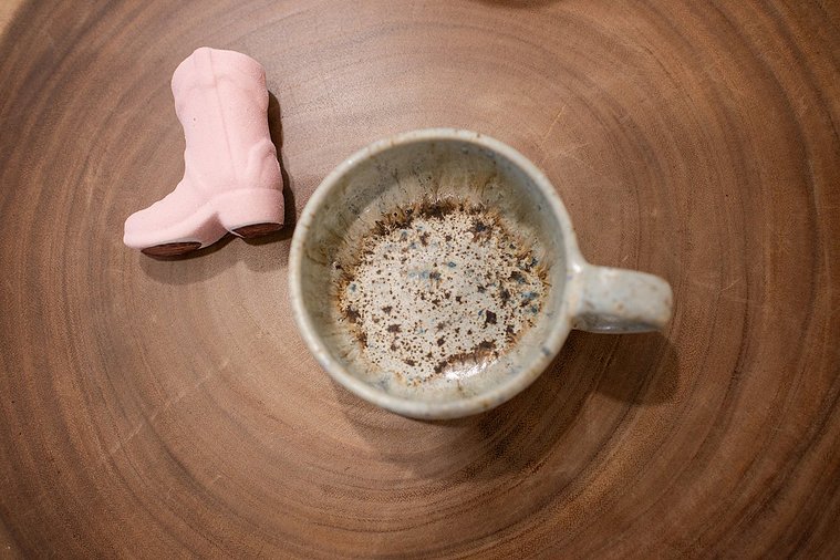 close up branding image of an empty coffee cup with a small pink cowboy boot decor piece next to it against a woodgrain table at a graphic design team branding session in OKC