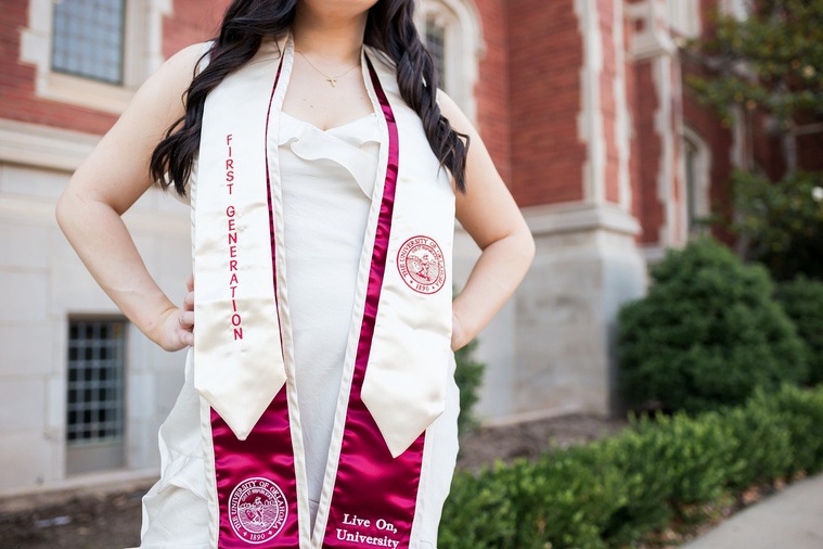 close up shot of a university of oklahoma graduation stole on a college senior girl with hands on hips, standing in front of Bizzell Library on OU campus in Norman
