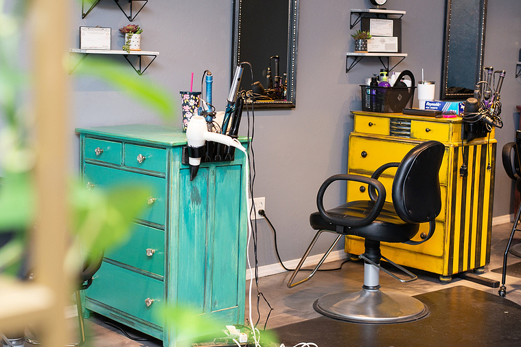a hair stylist's station with a bright green and yellow cabinet with a chair and hair tools around with green plants in foreground at a branding session at Vibe Beauty Bar in Tuttle, Oklahoma