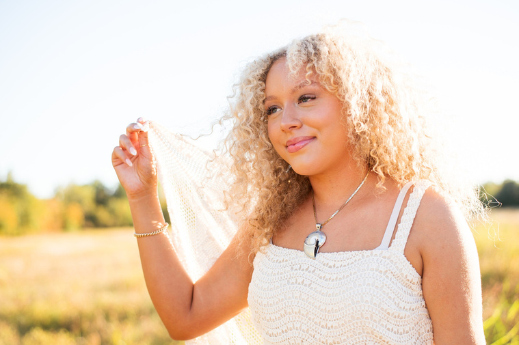 close up portrait of a high school senior girl with blonde curly hair and blue eyes wearing a white dress holding a blanket behind her and and smiling softly to the side at Martin Nature Park in Oklahoma City