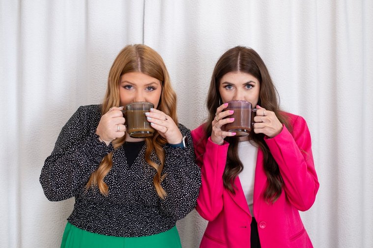 fun team photo of two young women wearing professional attire sipping coffee and looking cutely at camera at a graphic design team branding session in OKC