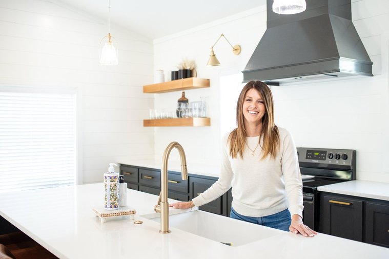 Brand photo shoot of realtor in OKC. She stands behind a kitchen island with a big friendly smile as she shows the kitchen to her clients