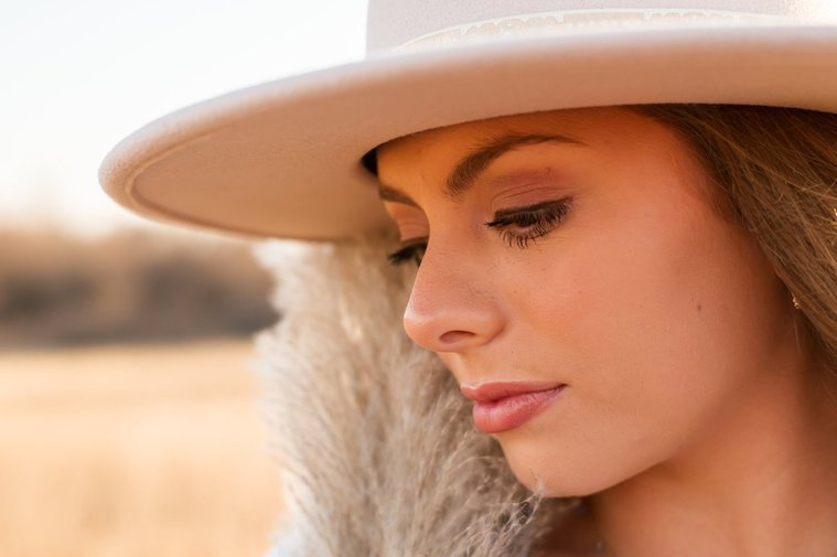 close up profile shot of a senior girl wearing a western hat holding pampa grass along her face looking down softly