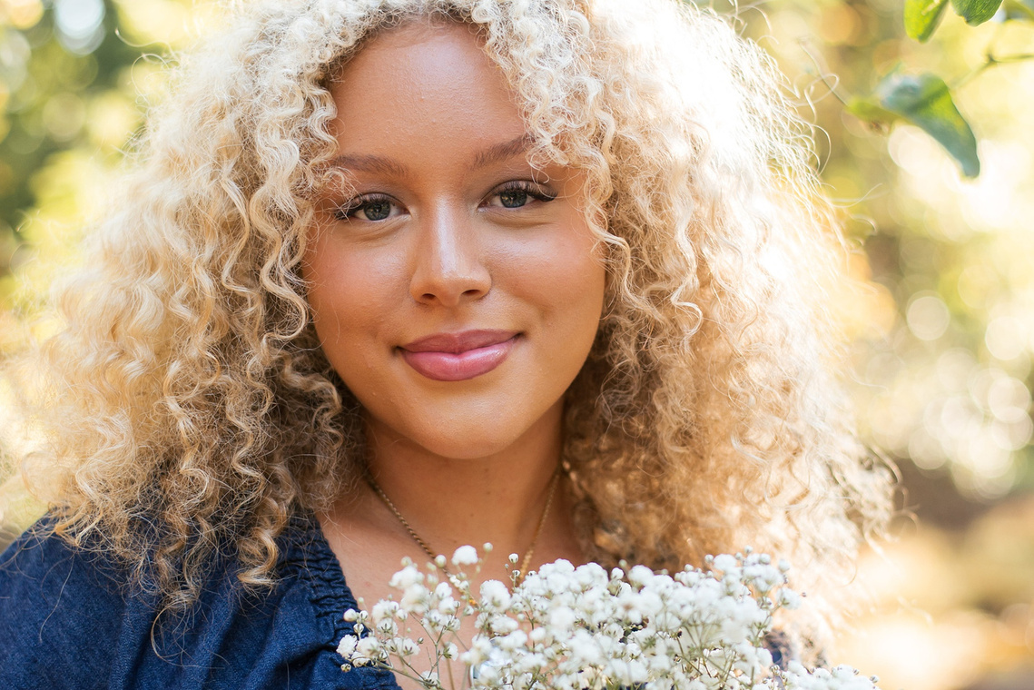 close up portrait of a high school senior girl with blonde curly hair and blue eyes holding a bouquet of baby's breath and smiling softly at Martin Nature Park in Oklahoma City
