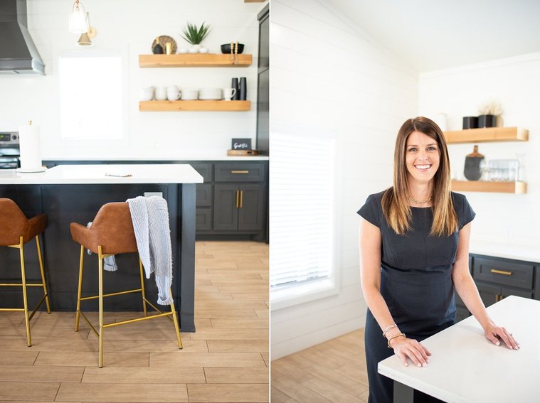 Brand photo shoot of realtor in OKC. She stands in a kitchen in a professional black dress and smiles. Detailed photo showing lived-in home with island chair pulled out and a sweater draped over it.
