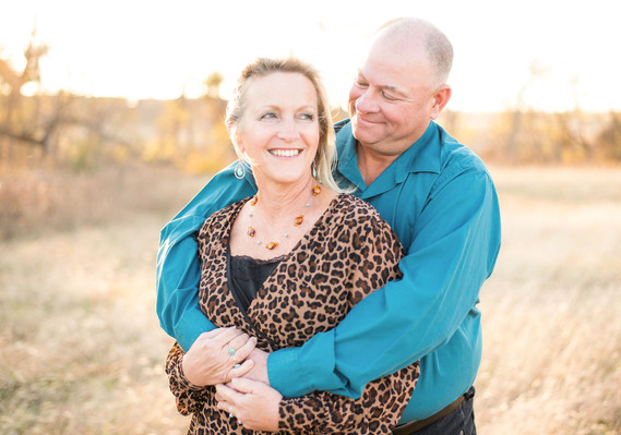A husband has his arms wrapped around his wife and they are smiling at each other