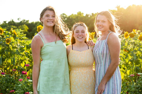 Three teenage girls pose in front of a flower field in rural Oklahoma at sunset