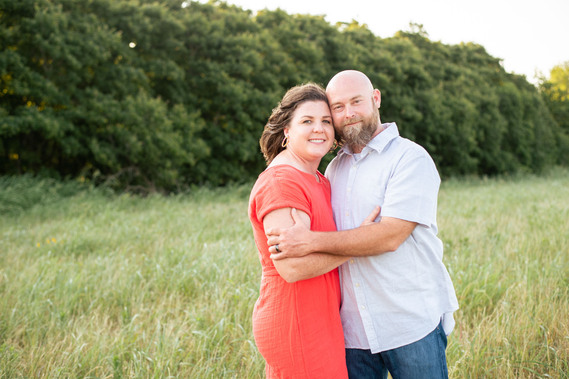 A husband and wife pose in front of a grassy meadow at sunset in Oklahoma