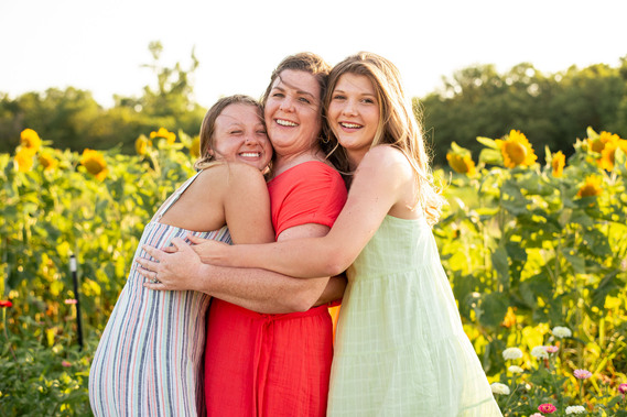 A mother and her two teenage daughters pose in front of a flower field in rural Oklahoma at sunset