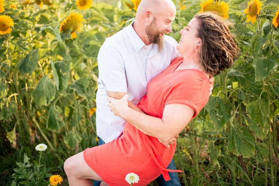 A husband and wife pose in front of a flower meadow at sunset in Oklahoma