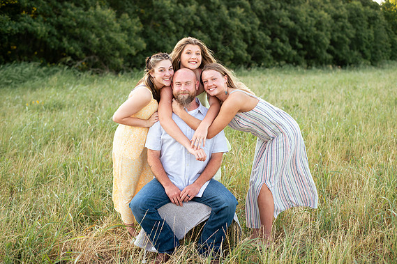 A father and his three teenage daughters pose in front of a grassy field in rural Oklahoma at sunset