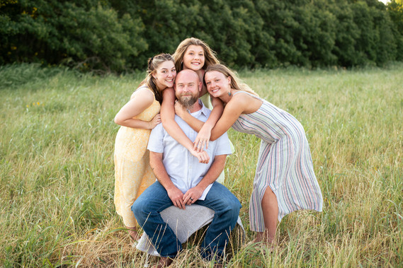 A father and his three teenage daughters pose in front of a grassy field in rural Oklahoma at sunset