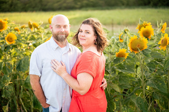 A husband and wife pose in front of a flower meadow at sunset in Oklahoma