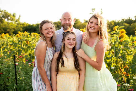 A father and his three teenage daughters pose in front of a flower field in rural Oklahoma at sunset