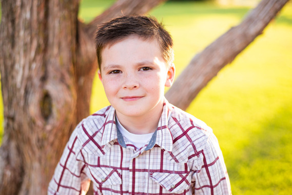 A little boy is in front of a tree and smiling in his back to school photo session in the country in Oklahoma