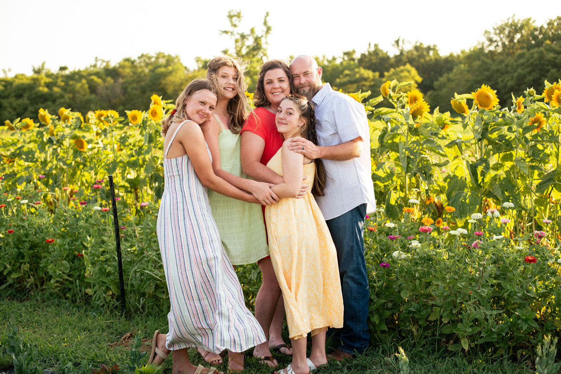 Parents and their three teenage daughters pose in front of a flower meadow at sunset in Oklahoma