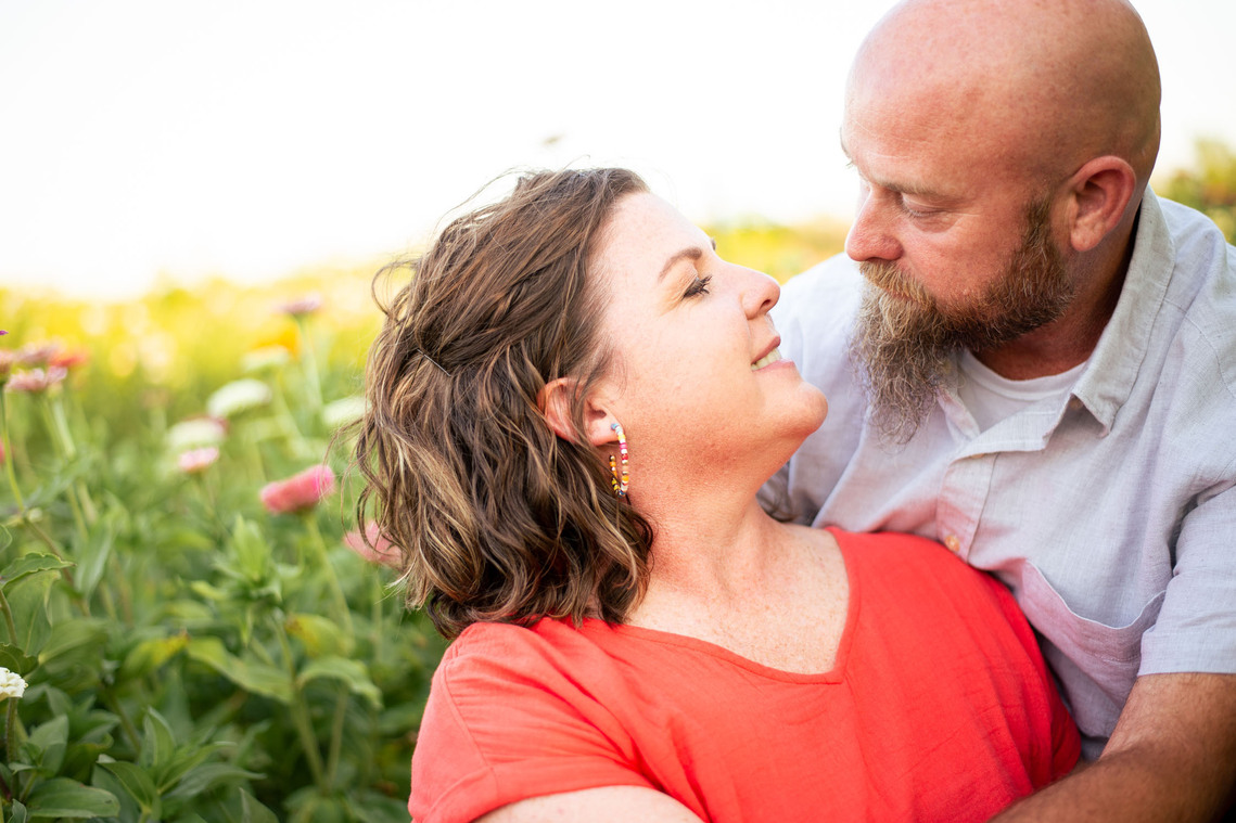 A husband and wife pose in front of a flower meadow at sunset in Oklahoma