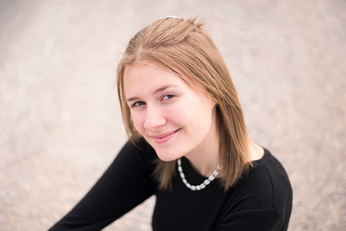 Portrait of a teenage girl in a black t-shirt sitting on the ground and soft smiling at the camera.