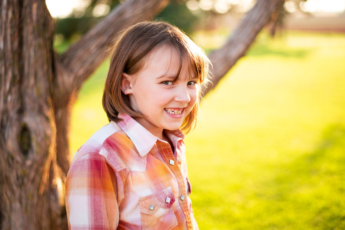 A little girl smiles in front of a tree at her back to school photo session in the country in Oklahoma