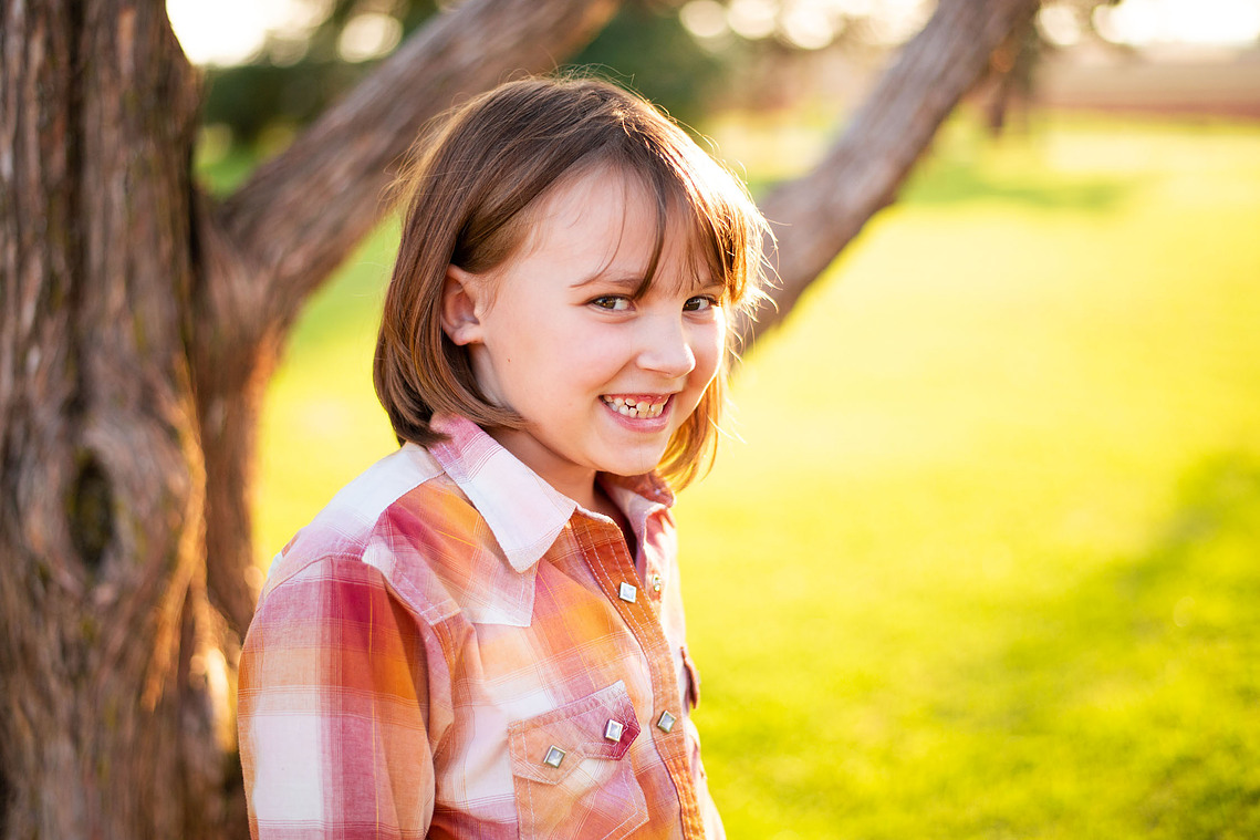 A little girl smiles in front of a tree at her back to school photo session in the country in Oklahoma