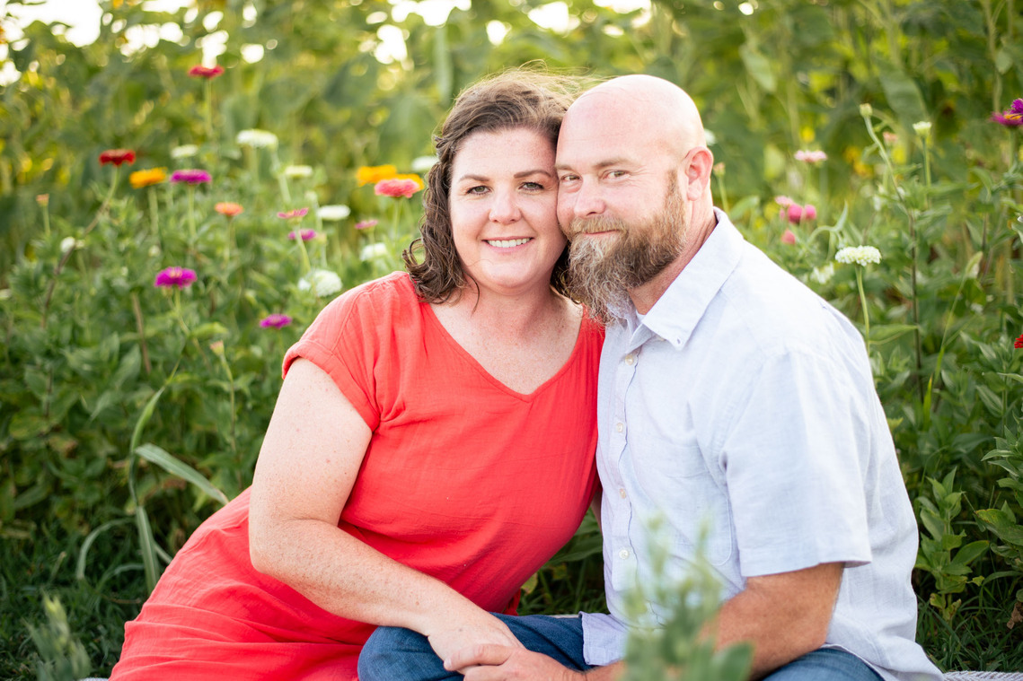 A husband and wife pose in front of a flower meadow at sunset in Oklahoma