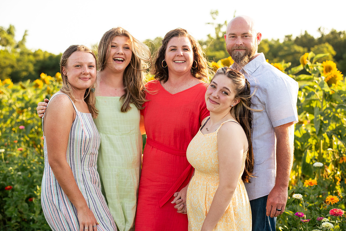 Parents and their three teenage daughters pose in front of a flower meadow at sunset in Oklahoma