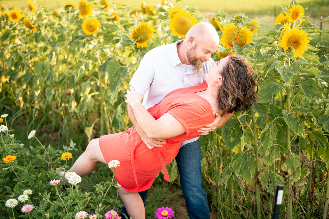 A husband dips his wife in a photography pose in front of a flower meadow at sunset in Oklahoma