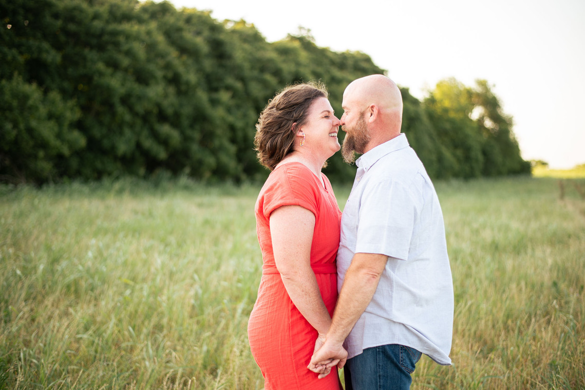 A husband and wife pose in front of a grassy meadow at sunset in Oklahoma