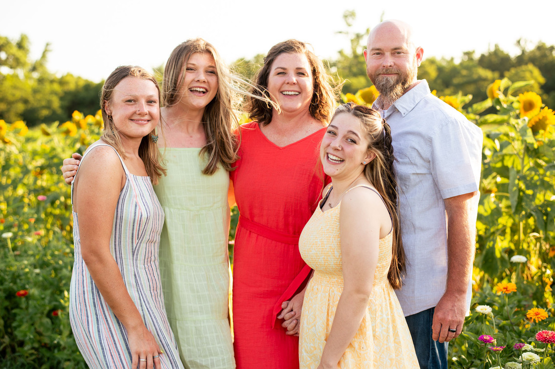 Parents and their three teenage daughters pose in front of a flower meadow at sunset in Oklahoma