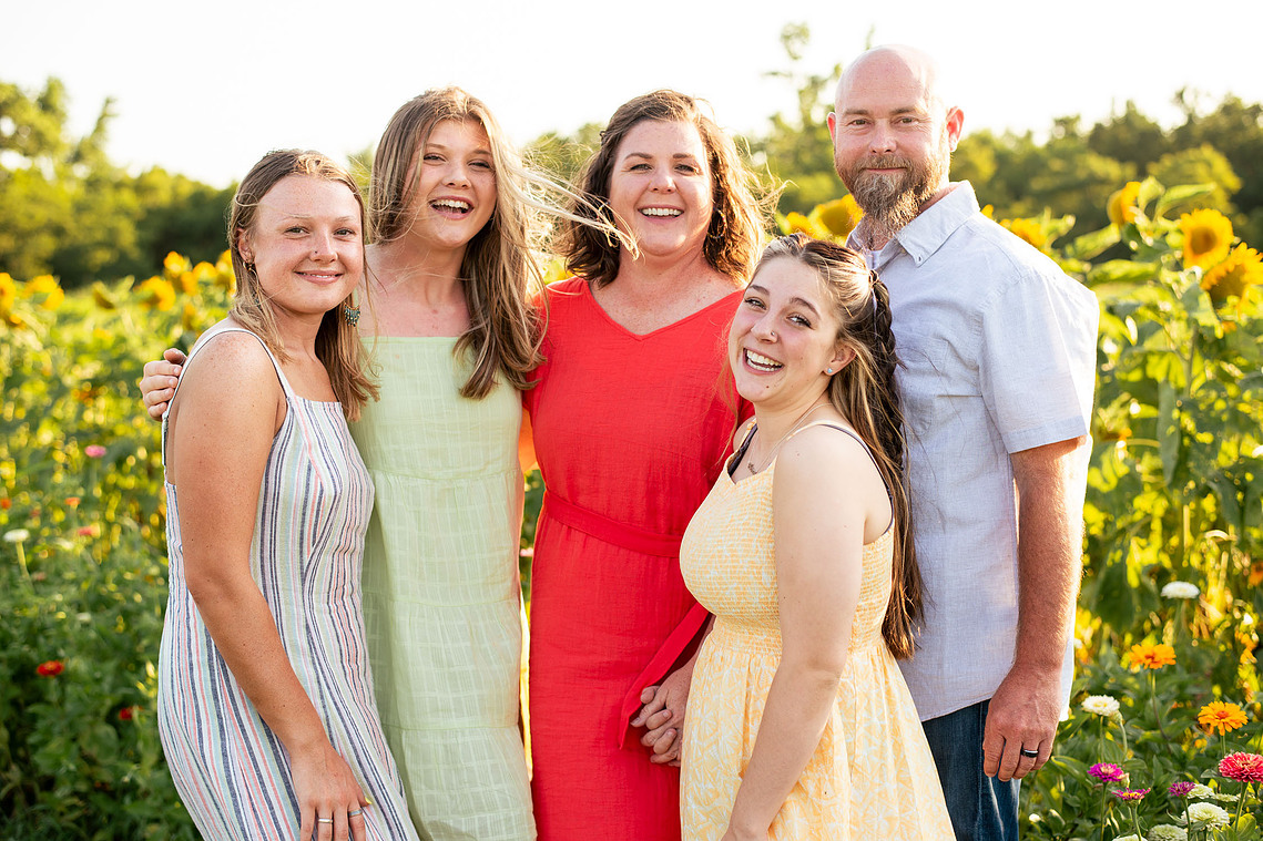 Parents and their three teenage daughters pose in front of a flower meadow at sunset in Oklahoma