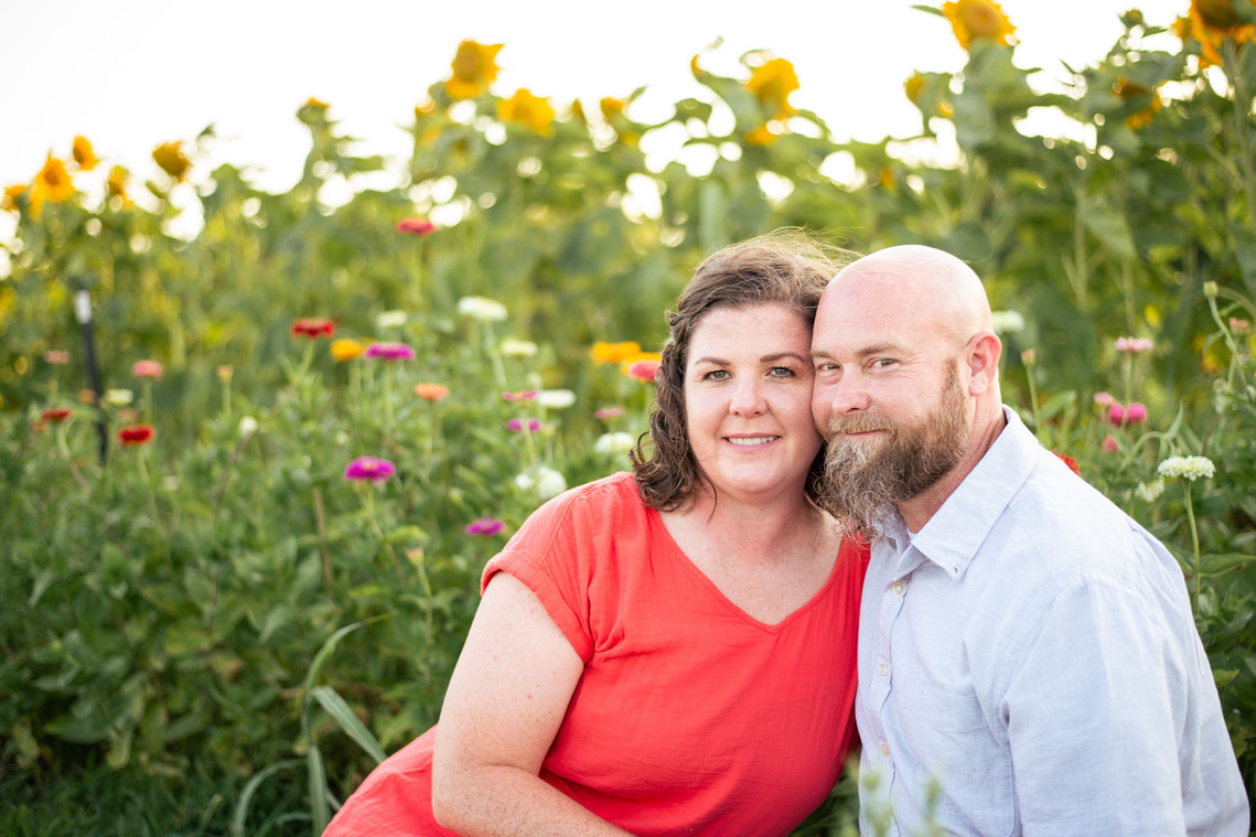 A husband and wife pose in front of a flower meadow at sunset in Oklahoma