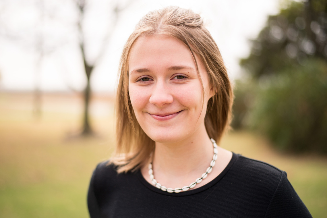 portrait of a teenage girl in a black shirt in a park smiling softly at the camera