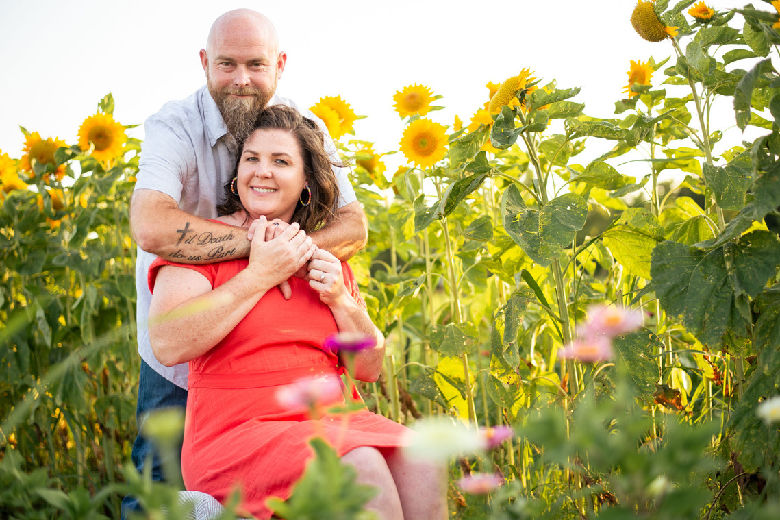 A husband and wife pose in front of a flower meadow at sunset in Oklahoma