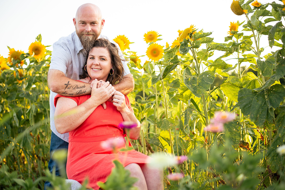 A husband and wife pose in front of a flower meadow at sunset in Oklahoma